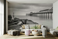Rugged, textured rocks are prominent in the foreground, leading the eye towards the pier.
