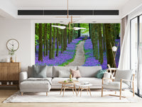 Nature wallpaper with tall forest trees and a carpet of purple-blue bluebells along a peaceful path.