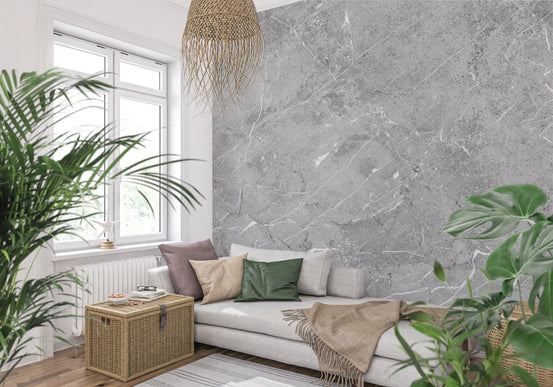 Sunny living nook with gray sofa, wicker trunk and palms on gray marble wallpaper GD14083