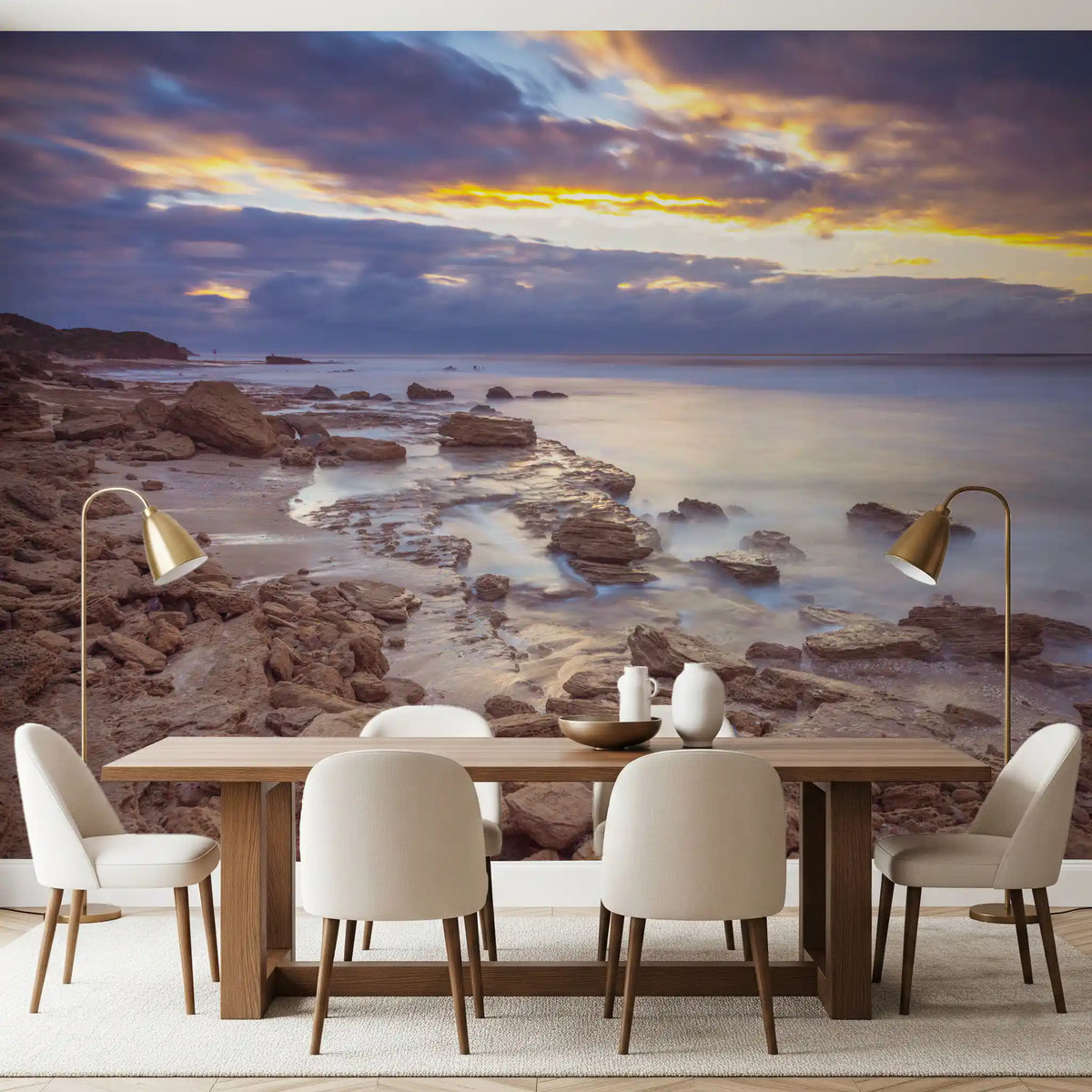 Beach wallpaper behind a long wood dining table with cream chairs and brass lamps GD14207