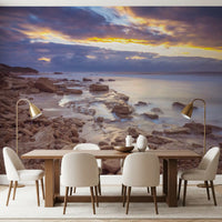 Beach wallpaper behind a long wood dining table with cream chairs and brass lamps GD14207