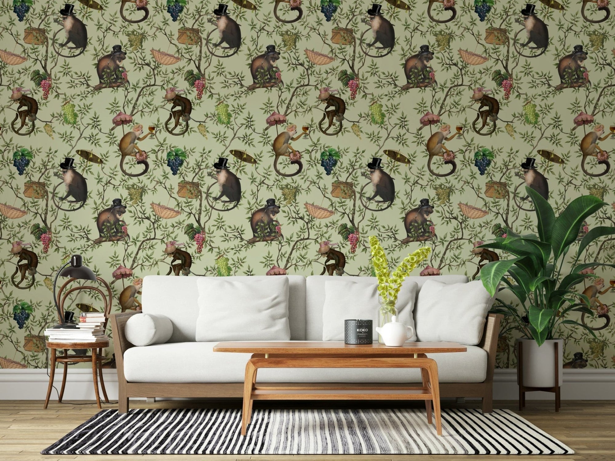 A Primate's Afternoon Tea green wallpaper behind a white wood-frame sofa with a striped rug and plant