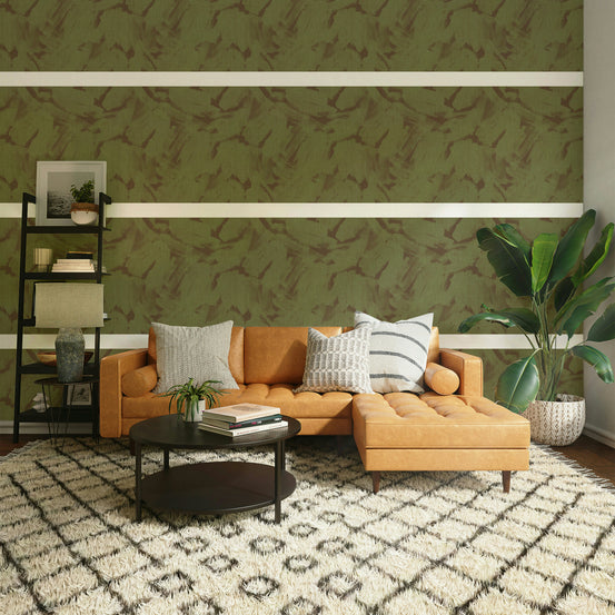 Acrylic Abstract Brushstroke Textured Camo wallpaper in olive green and brown behind a tan leather sectional in a living room