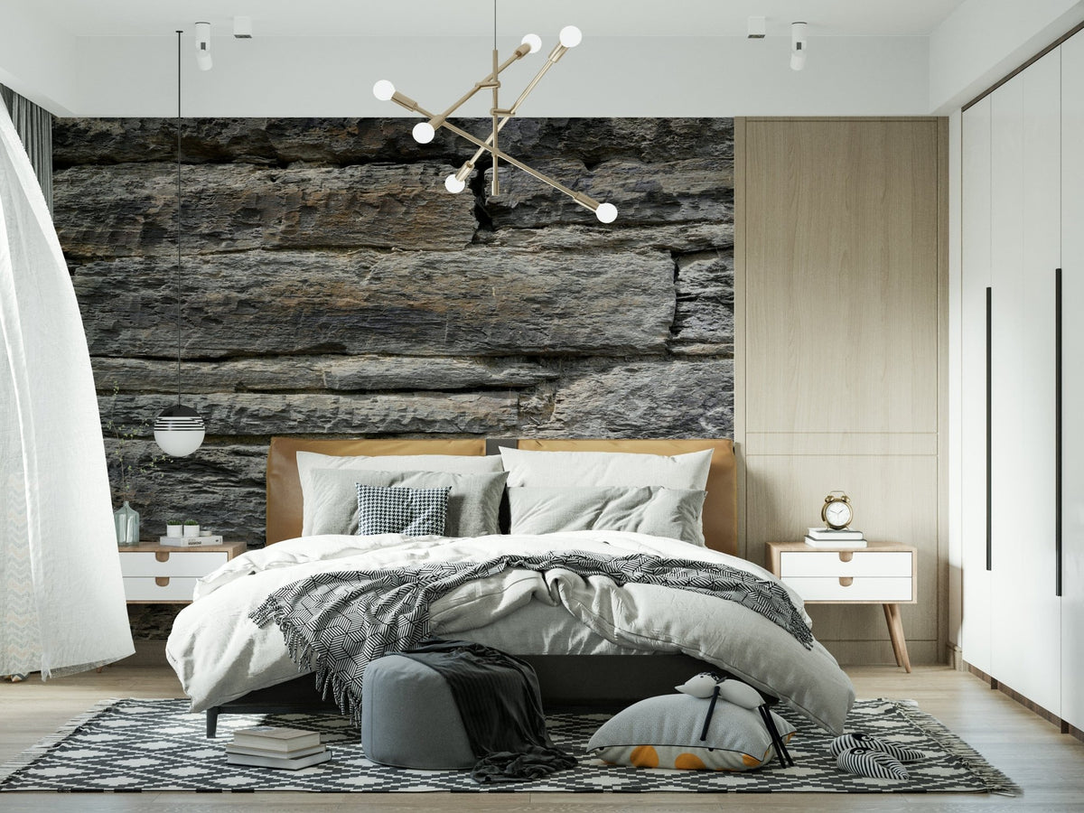 Aged Stone wallpaper mural of layered grey rock above a wood-headboard bed lit by a gold sputnik chandelier