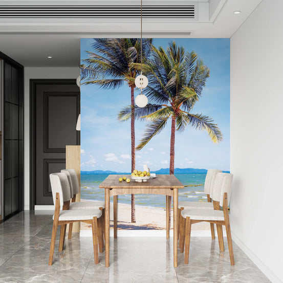 Beachfront Bliss wallpaper mural of two palm trees on a tropical beach behind a wood dining table and cream chairs