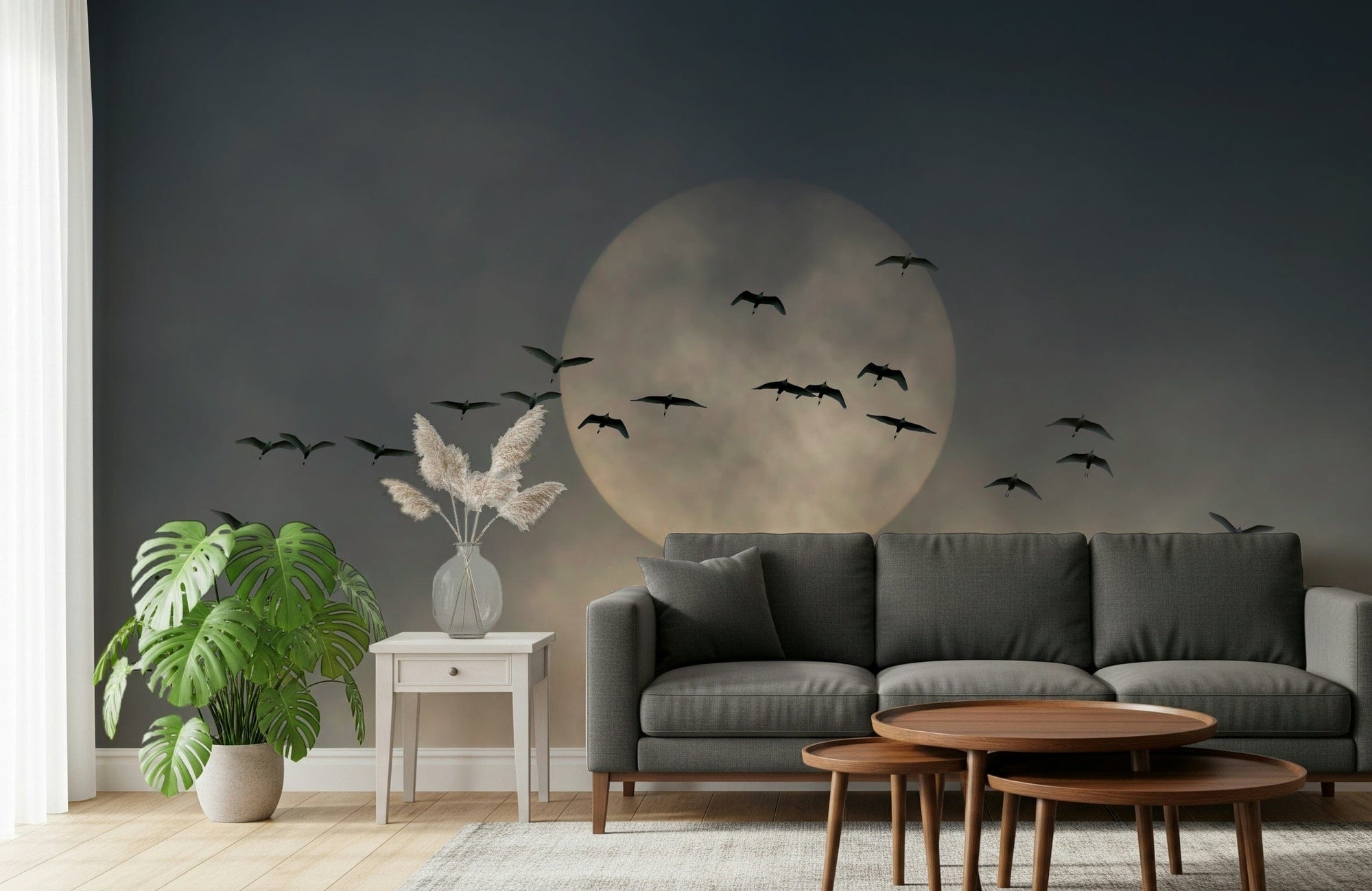 Soaring Souls wallpaper mural of birds flying past a pale moon behind a charcoal grey sofa in a living room