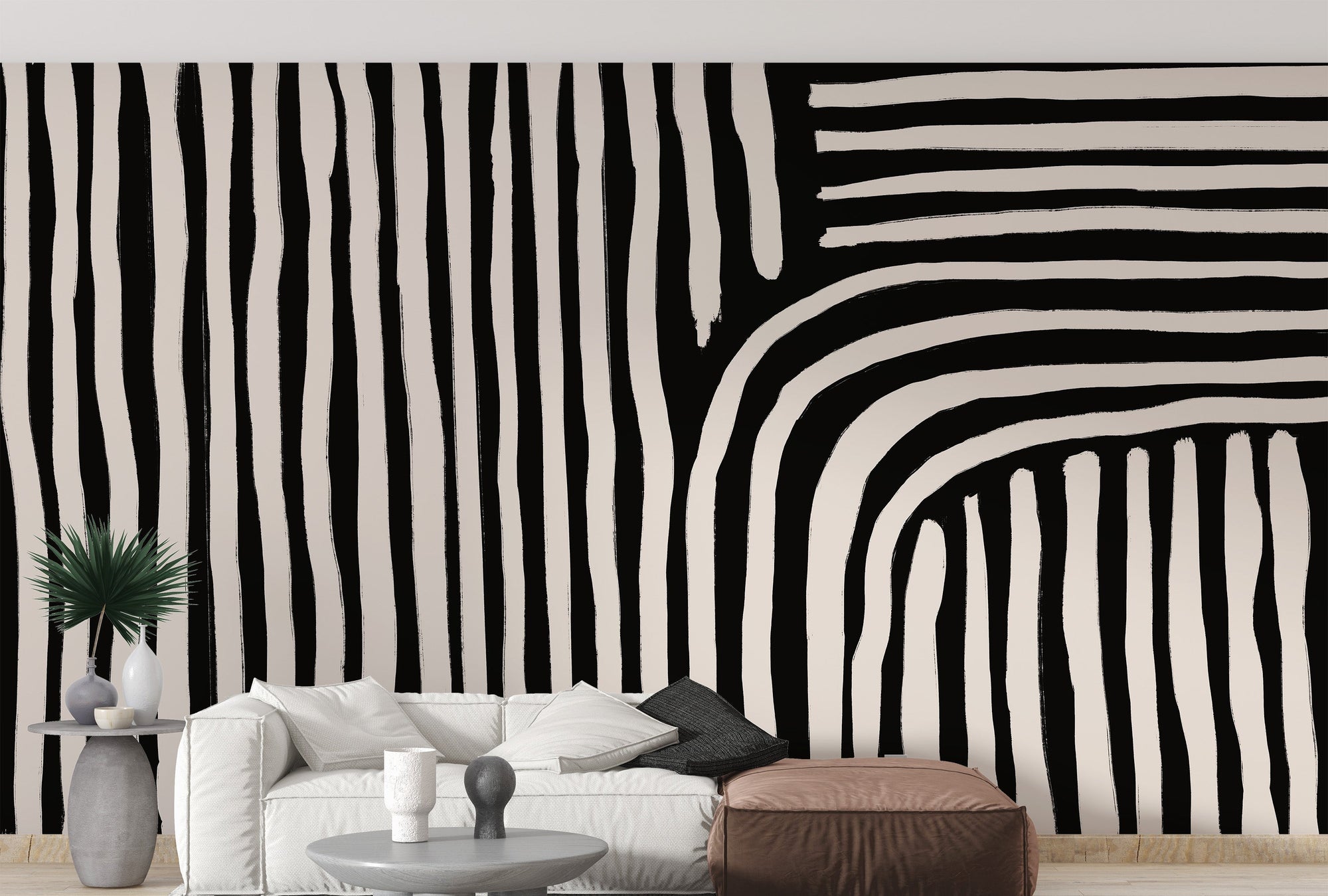 Black and white striped wallpaper mural of wavy painted lines behind a white sofa and brown pouf in a living room