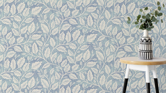 Blue Budding Branches wallpaper with cream leafy vines on dusty blue behind a white round stool and patterned vase