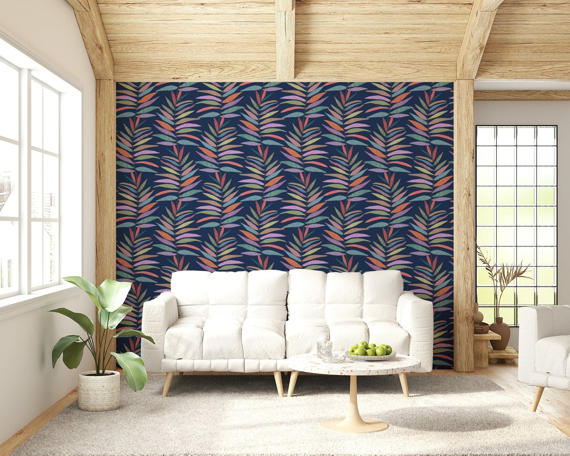 Botanical Groove wallpaper of colorful leaf fronds on navy behind a white sofa under a wood-beam ceiling