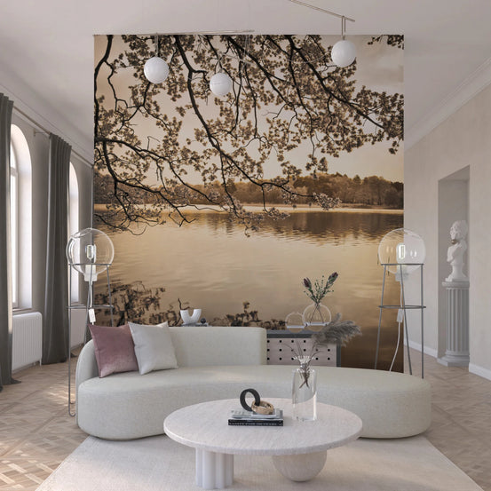 Branches above Lake wallpaper mural with sepia blossoms over a calm lake behind a curved cream sofa in a bright living room