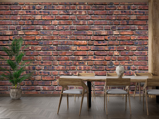 Heritage Brickwork wallpaper of weathered red brick behind a wood dining table and chairs with a potted palm