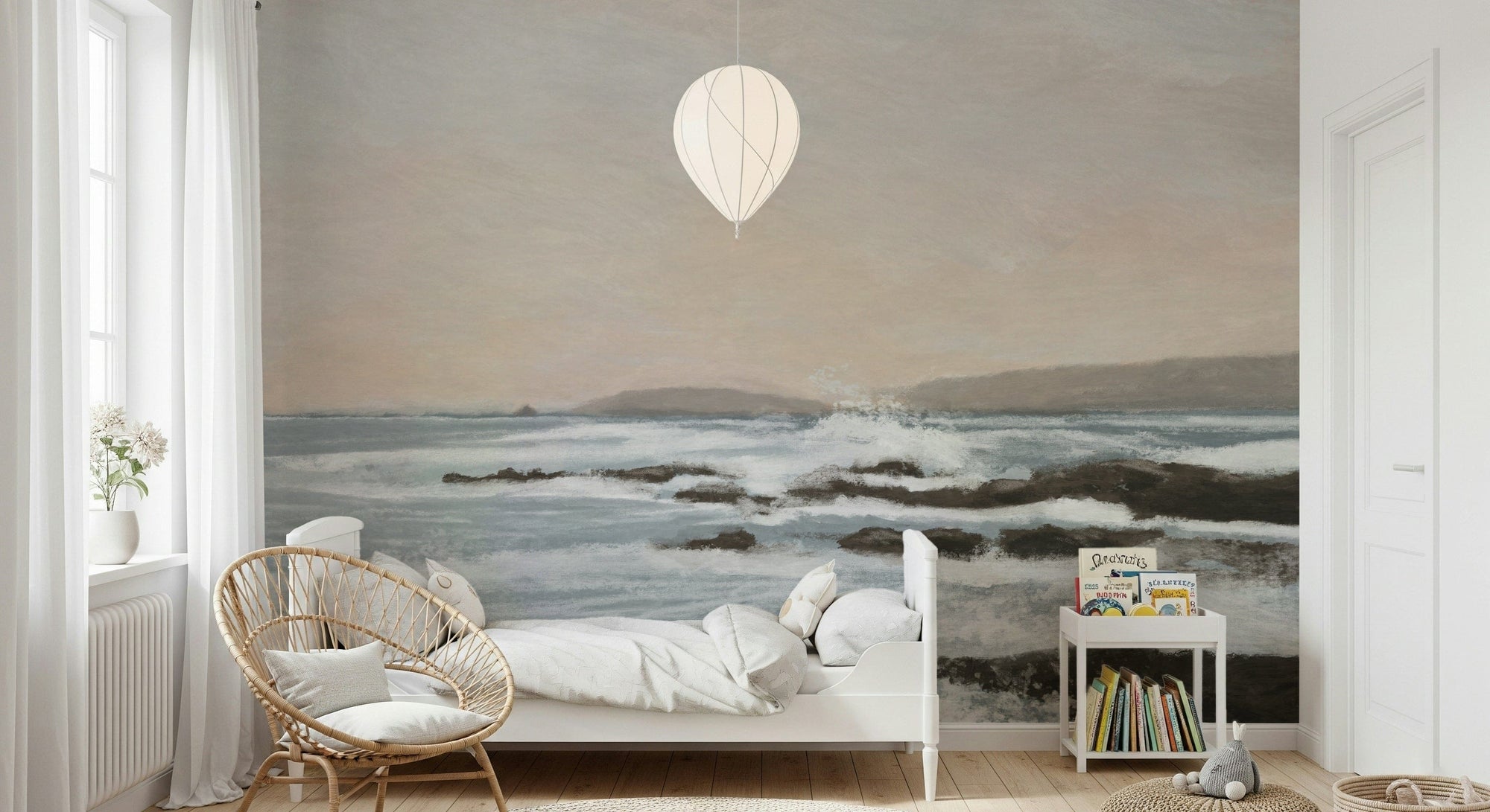 Coastal Hues wallpaper mural of soft blue waves and rocks behind a white bed and rattan chair in a nursery