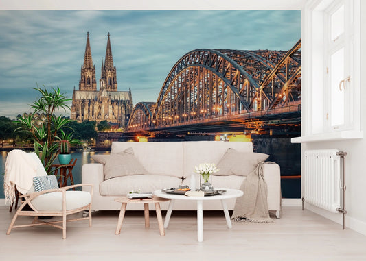 Cologne at Dusk wallpaper mural showing the lit bridge and cathedral above a cream sofa and wooden armchair in a living room