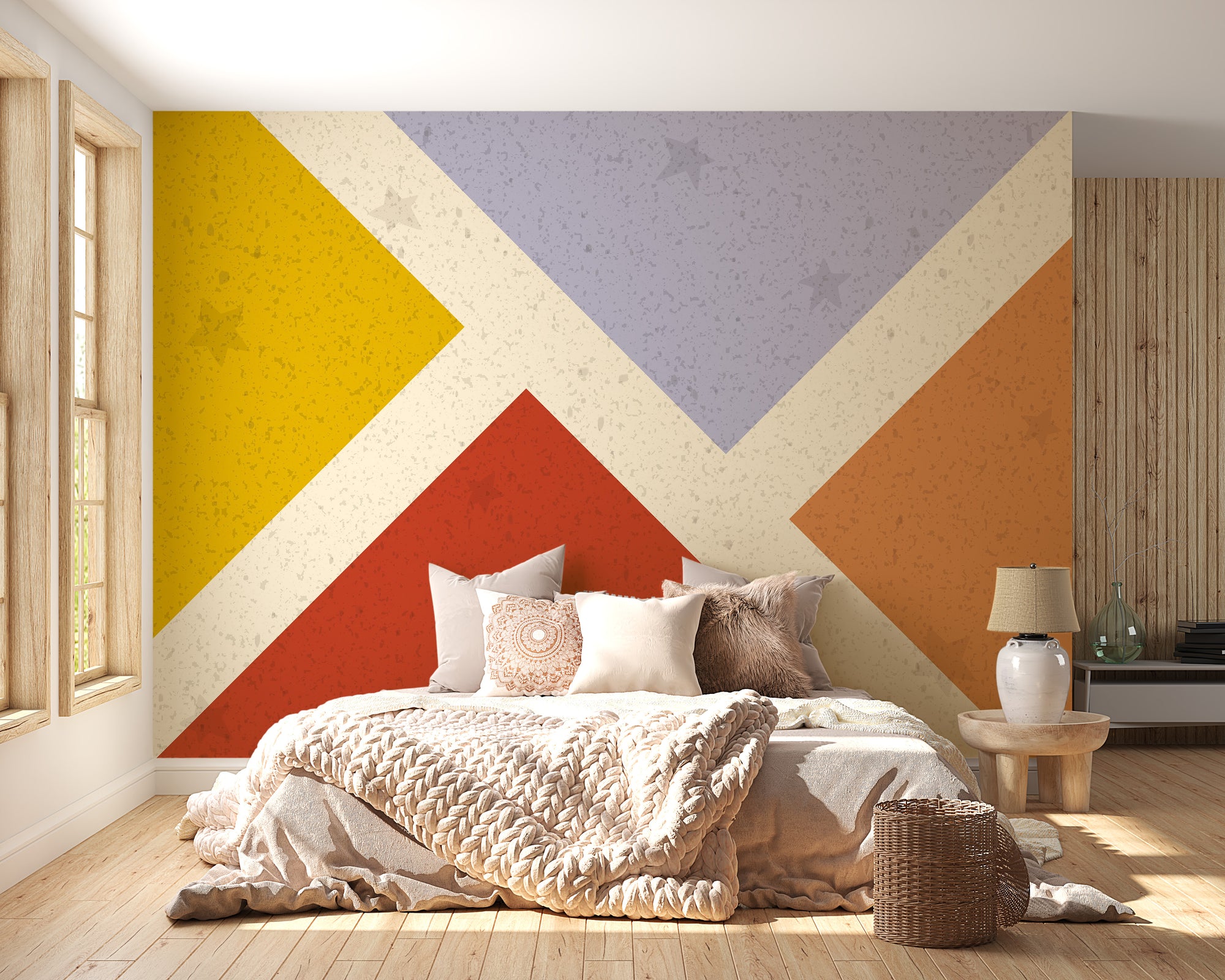 Colorful square design wallpaper mural with bold yellow, red and orange triangles behind a low bed and cream knit throw