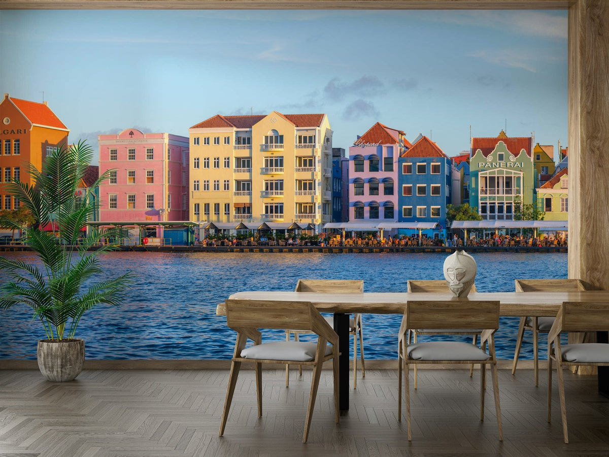 Willemstad Waterfront wallpaper mural of colorful harbor houses behind a wooden dining table and chairs by the water