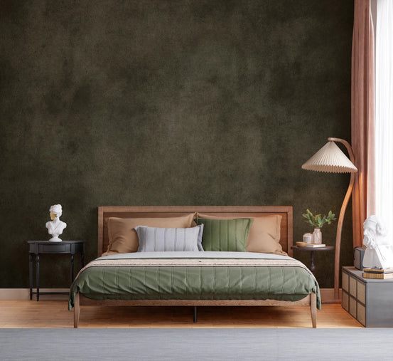 Dirty Paper Earth wall mural in dark olive plaster behind a wood bed with green bedding and a pleated floor lamp