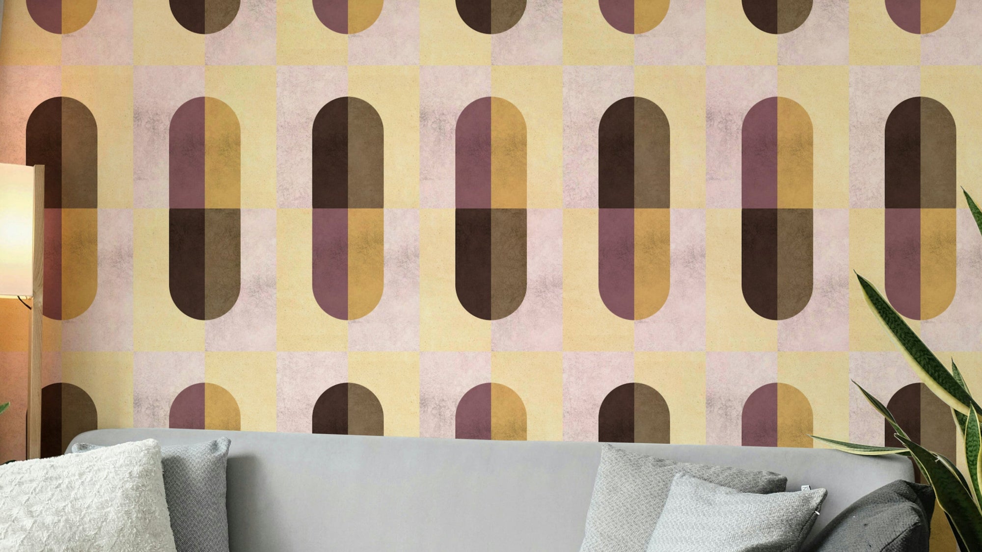 Earthy Geometric wallpaper in mustard, plum and brown capsule shapes above a grey sofa and snake plant