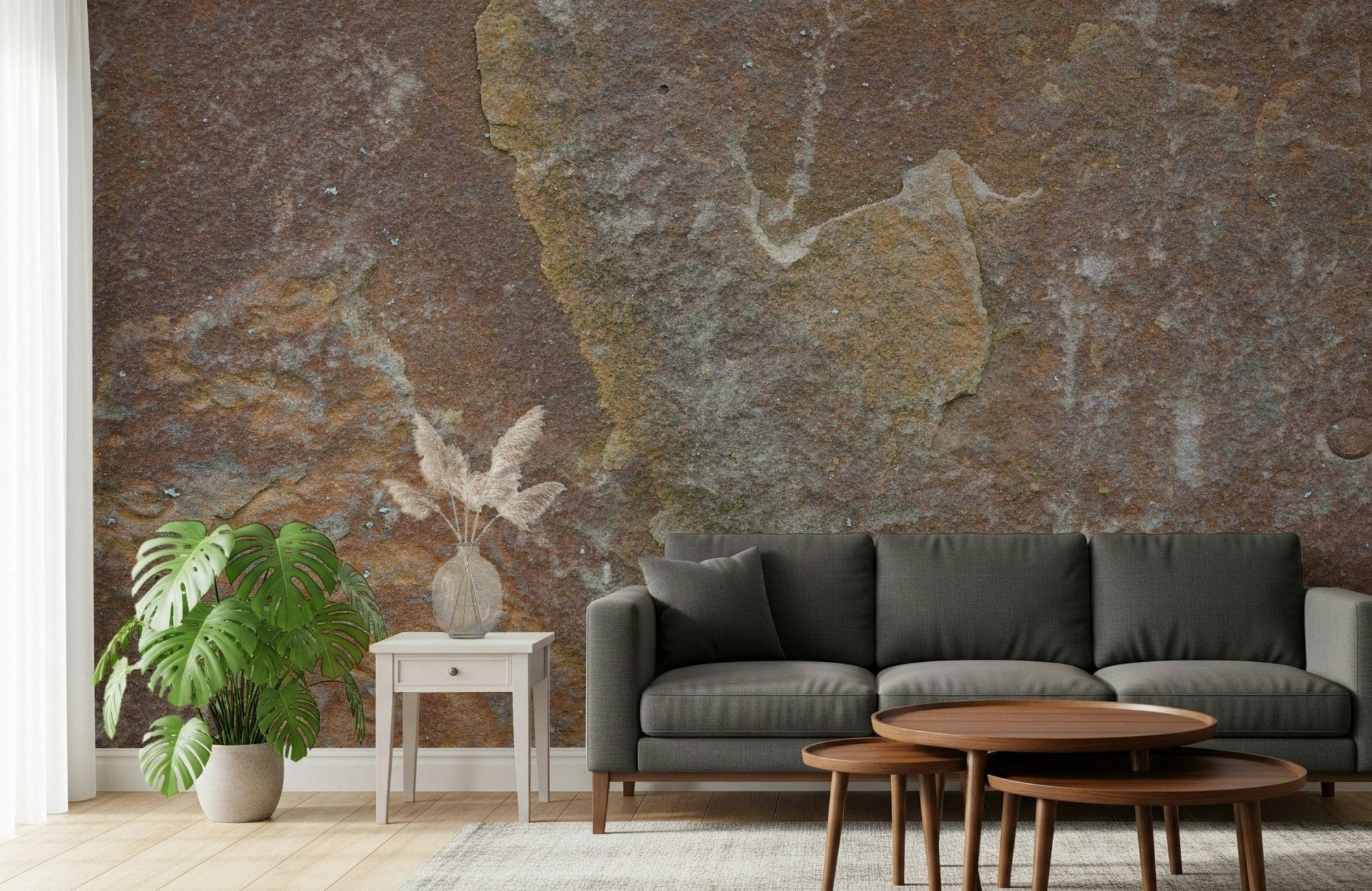 Earthy Stone Texture wallpaper mural of rust-brown stone behind a charcoal sofa and walnut nesting tables in a living room
