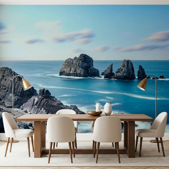 Ethereal Coastline wallpaper mural of blue sea stacks and cliffs behind a wood dining table and beige chairs in a dining room
