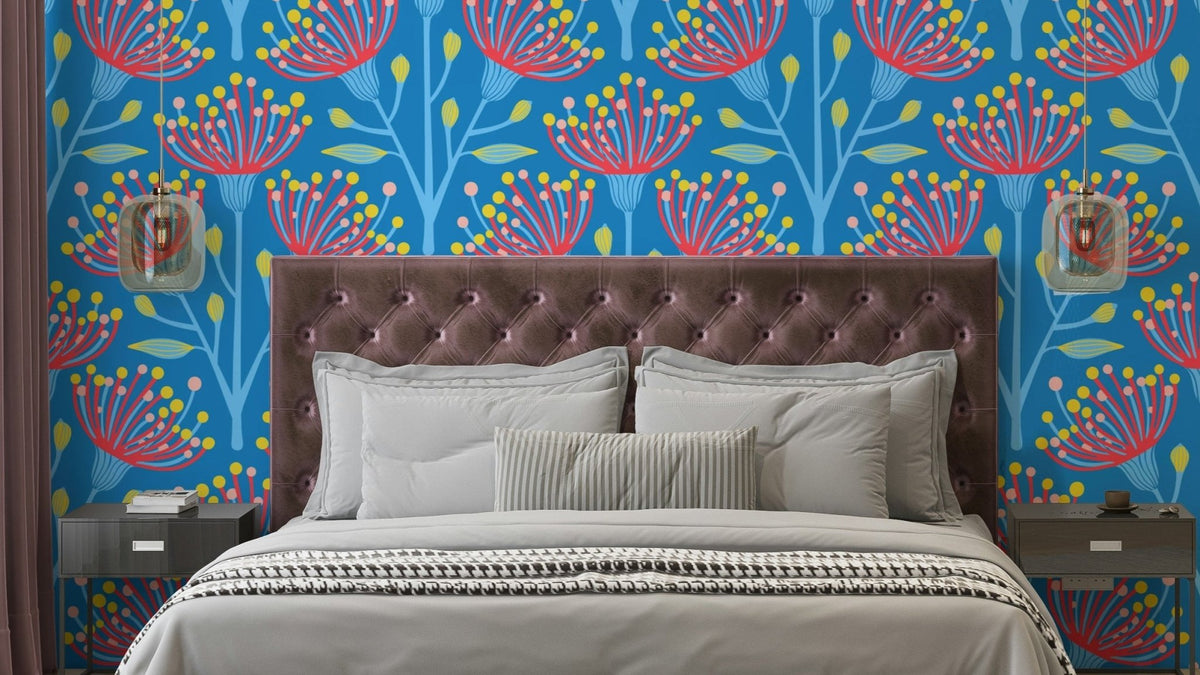 Eucalyptus floral wallpaper with red and yellow blooms on bright blue behind a mauve tufted headboard in a bedroom