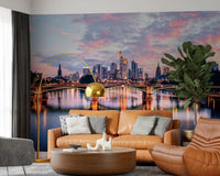 Frankfurt Dawn wallpaper mural of the glowing skyline and river behind a tan leather sofa and gold arc lamp