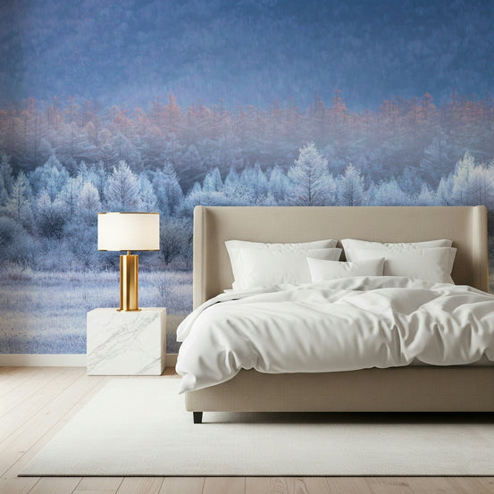 Frozen Dawn Vista wallpaper mural of a frosty blue forest at dawn behind a beige headboard bed with gold lamp