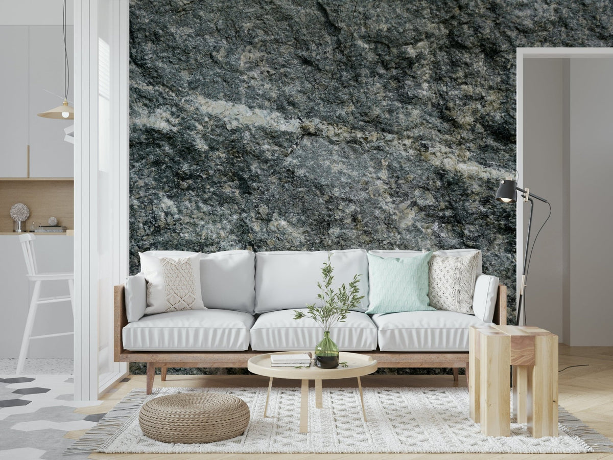 Granite grey wallpaper mural behind a white wood-framed sofa with a jute pouf in a living room