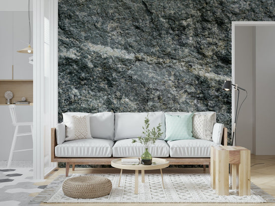 Granite grey wallpaper mural behind a white wood-framed sofa with a jute pouf in a living room
