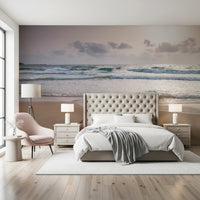 Happy Beach Vibes wallpaper mural of seaside waves behind a tufted cream bed and pink chair in a bedroom