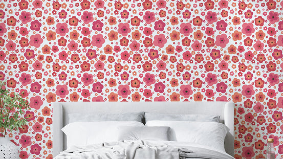 Happy Retro Blooms wallpaper of pink and coral daisies behind a grey upholstered bed with white pillows in a bedroom