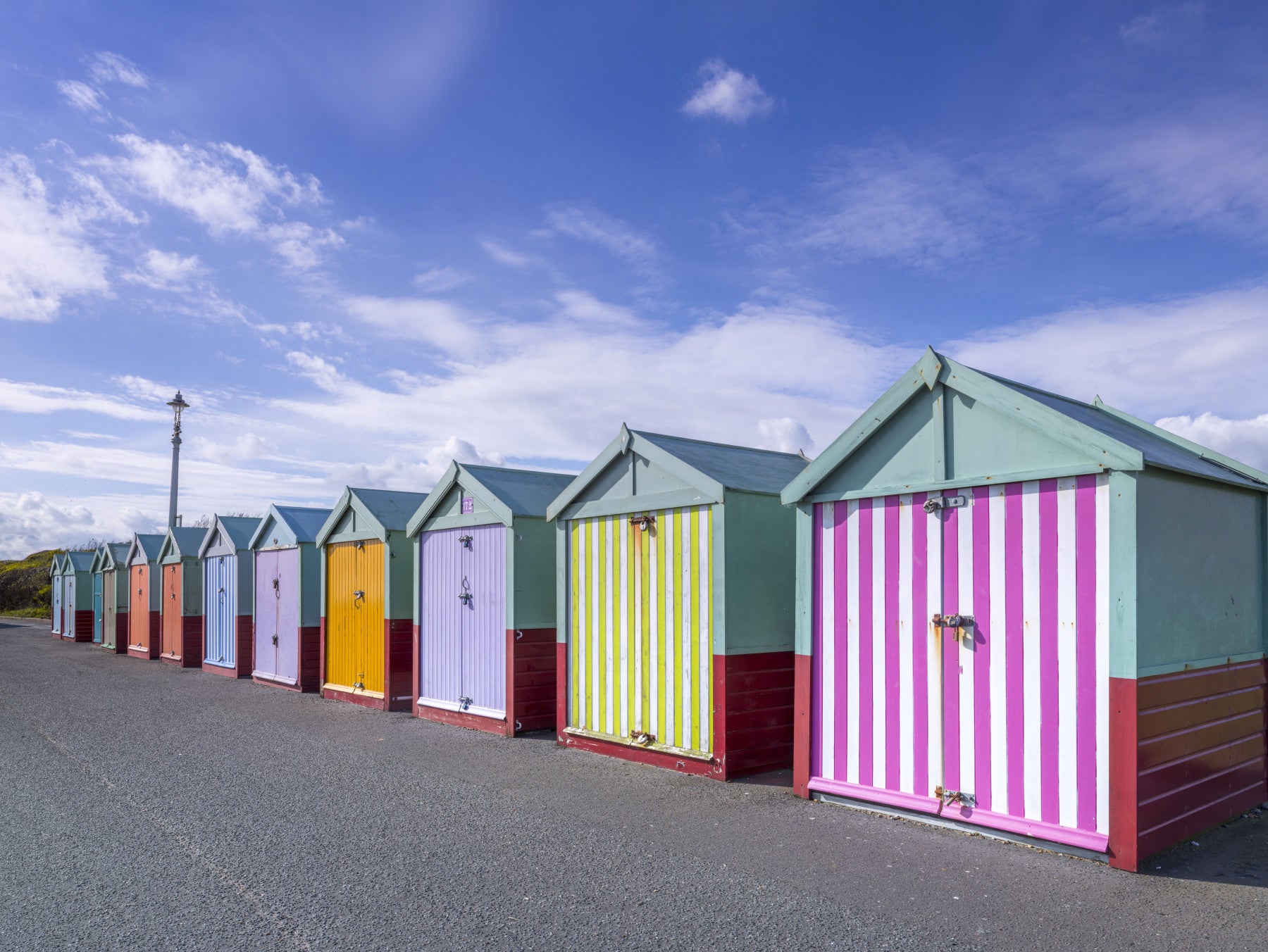 Beach huts mural in a girls bedroom with a white bed, rattan egg chair and bookshelf GD13132