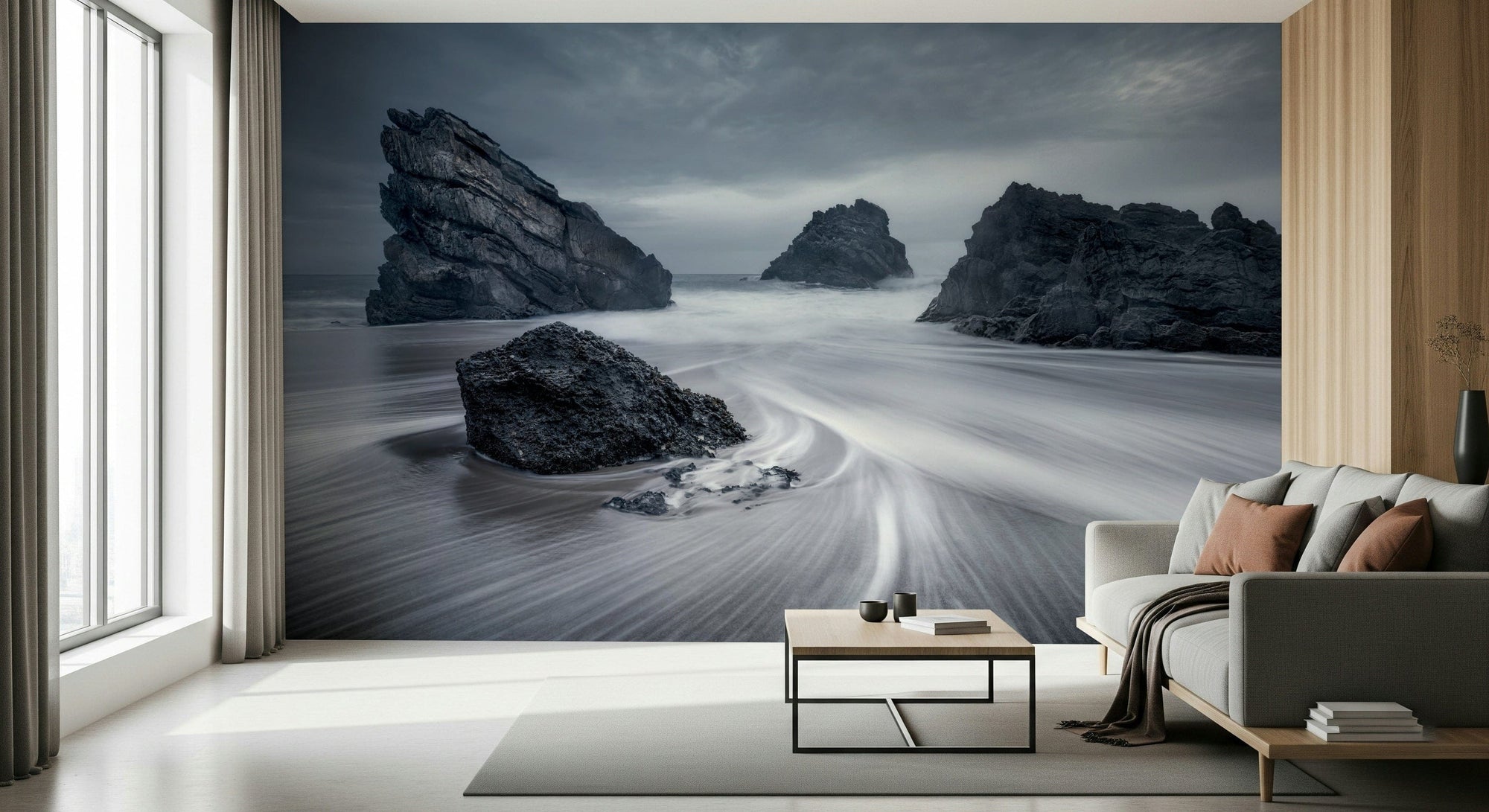Coastal Monoliths wallpaper mural of dark sea stacks on a misty beach behind a gray sofa in a living room