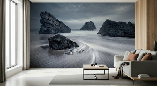 Coastal Monoliths wallpaper mural of dark sea stacks on a misty beach behind a gray sofa in a living room