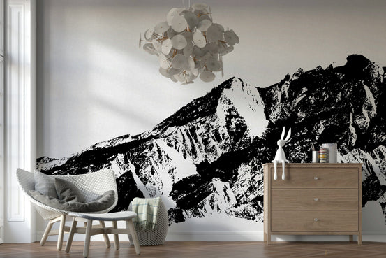 Monochrome Majesty wallpaper mural of a black and white mountain range behind a white rattan chair and wood dresser in a lounge