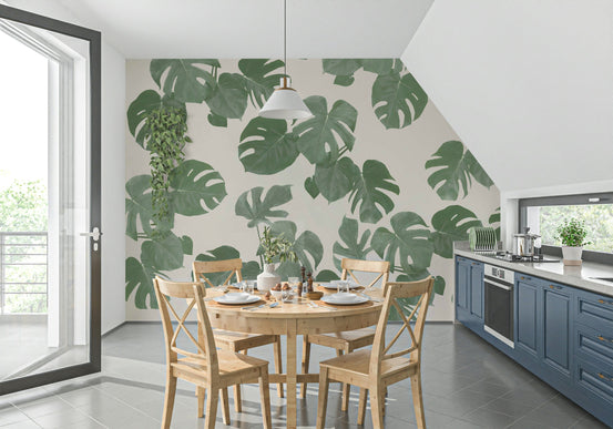 Monstera Dreams wallpaper mural with green palm leaves on cream behind a round wood dining table in a blue-cabinet kitchen