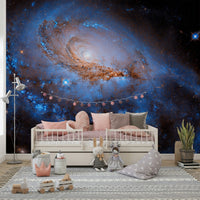 Nebula Dreams wall mural of a blue galaxy behind a white daybed with pink cushions and plush toys in a kids room