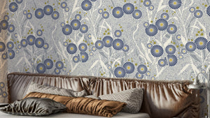 Nordic Petals wallpaper with blue floral blooms on grey behind a velvet headboard and pillows in a bedroom