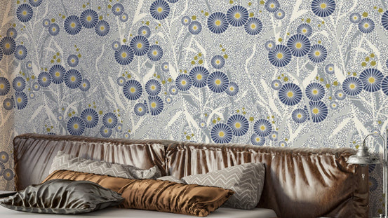 Nordic Petals wallpaper with blue floral blooms on grey behind a velvet headboard and pillows in a bedroom