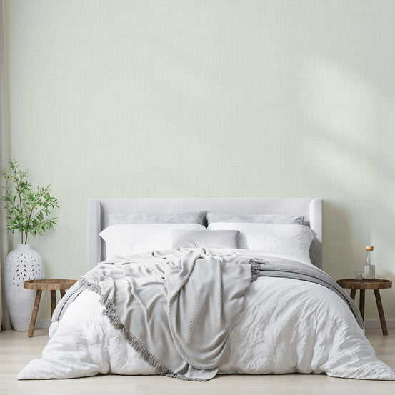 Old Canvas Cannoli Cream wallpaper in soft sage cream behind a grey upholstered bed with white bedding and olive plant