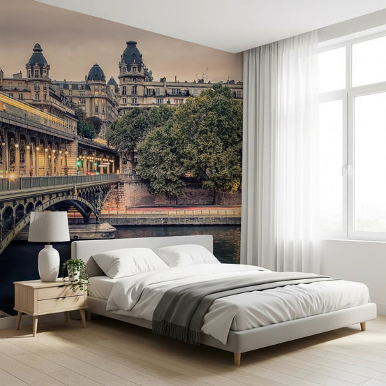 Parisian Bridge Lights wallpaper mural of the lit Bir-Hakeim bridge and Seine beside a white bed and wood nightstand in a bedroom