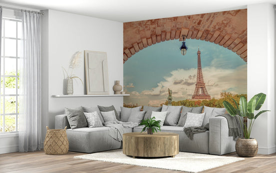 Parisian Vista wallpaper mural of the Eiffel Tower through a terracotta stone arch behind a grey sectional sofa in a living room