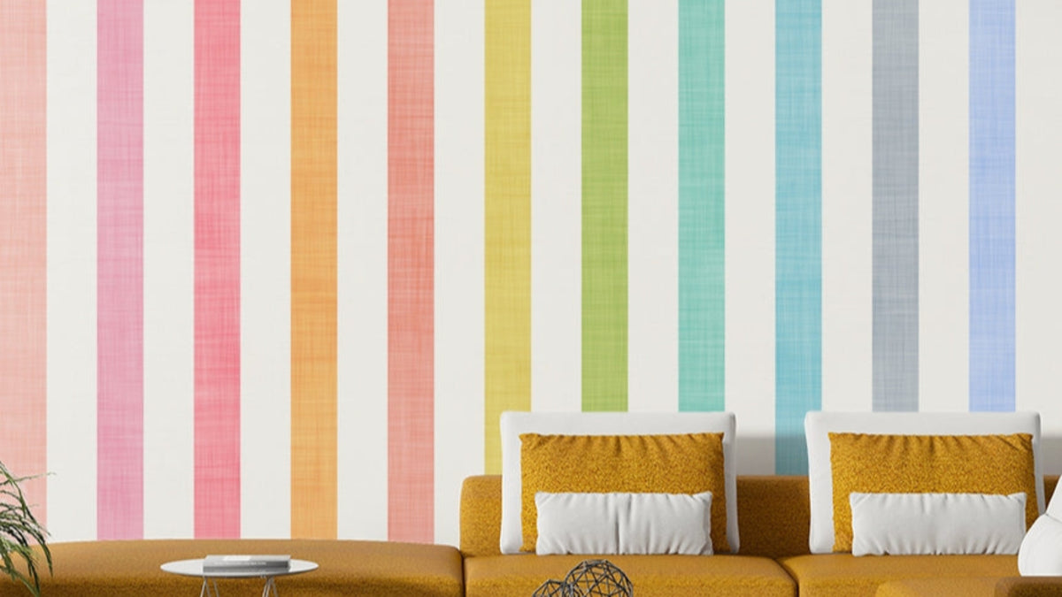 Pastel Breeze Vertical Stripes wallpaper in rainbow pastels behind a mustard sectional sofa in a living room