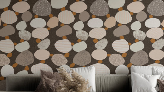 Chic Pebbled Elegance wallpaper with cream and brown pebbles on dark brown behind a grey sofa in a living room