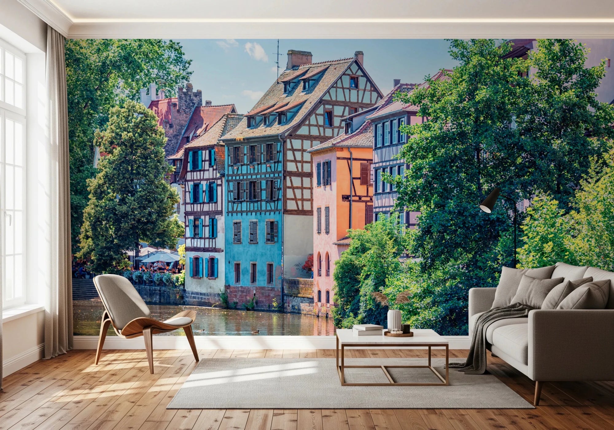 Petite France Charm wallpaper mural of colorful half-timbered canal houses behind a beige sofa and wood chair in a living room