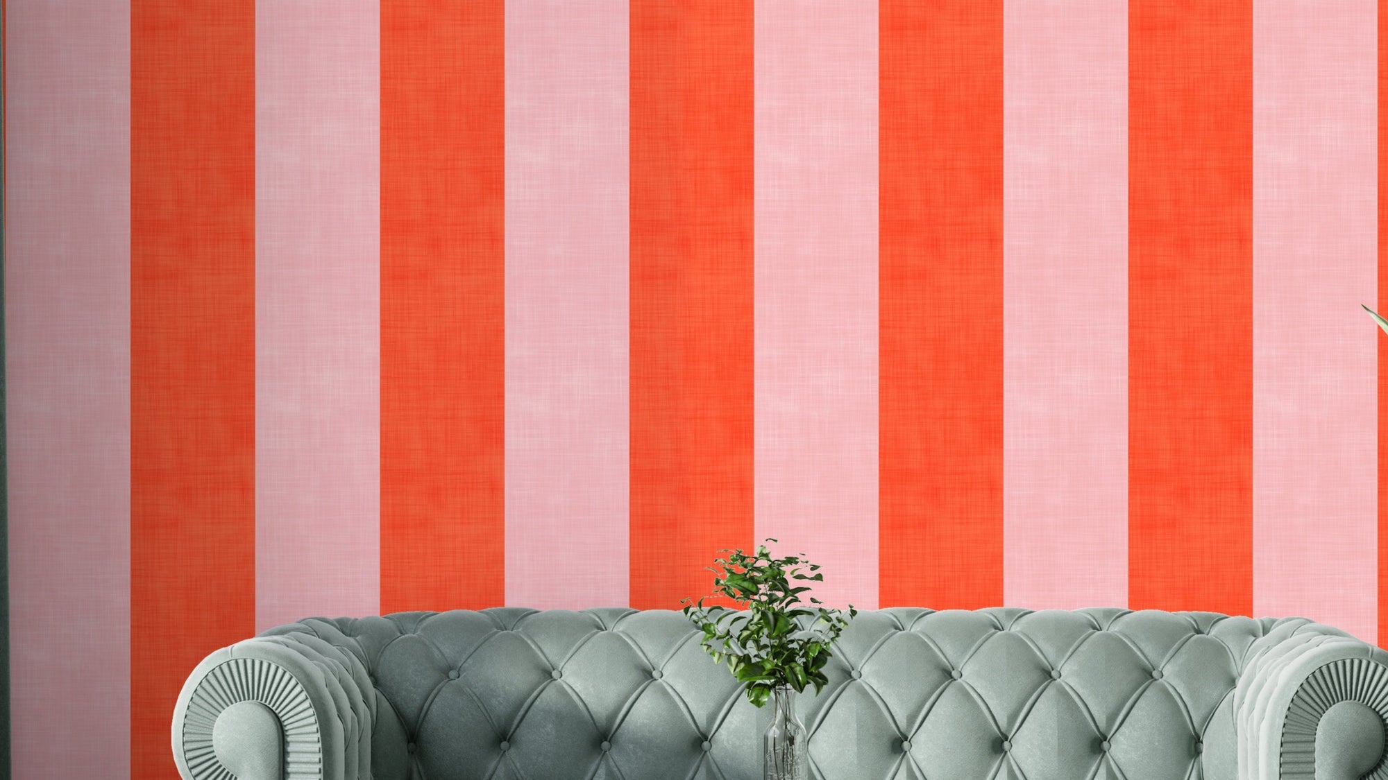 Pink and Red Stripes Linen Texture wallpaper behind a sage green tufted sofa with a glass vase in a living room