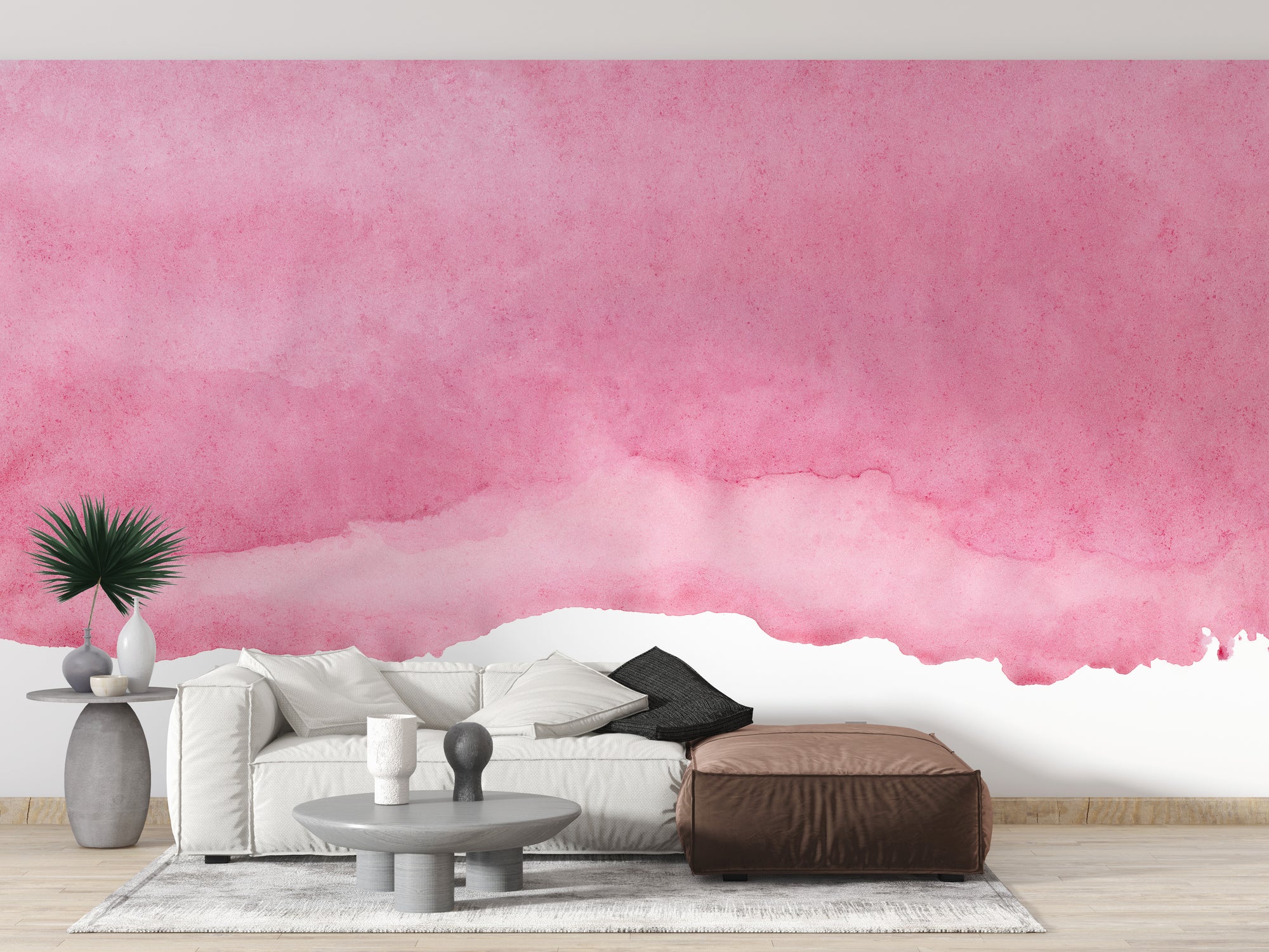 Pink shades watercolor wallpaper with a soft pink wash behind a white sofa and brown leather ottoman in a living room