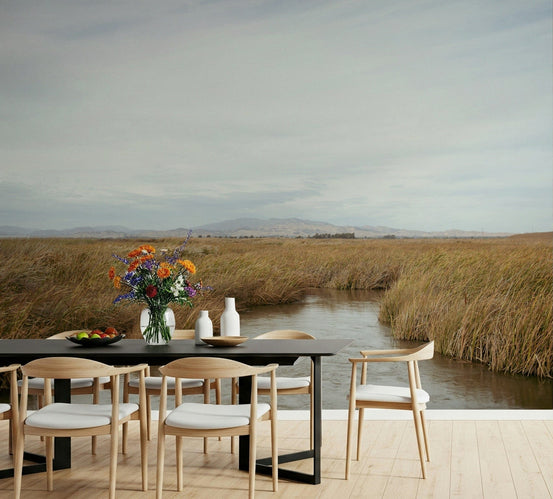 Tranquil Marsh View wallpaper mural of a golden reed marsh and water channel in a dining room with black table and wood chairs