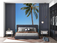 Tropical Retreat wallpaper mural of a beach palm and blue sea behind a navy upholstered bed in a bedroom