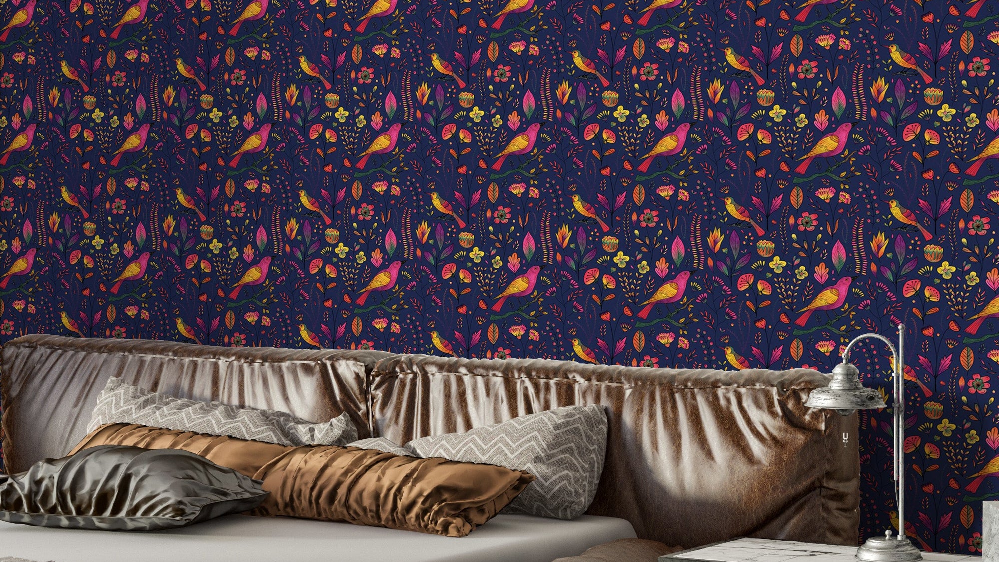 Whimsical Songbird Garden Navy wallpaper above a bed with satin gold and grey pillows and a vintage lamp