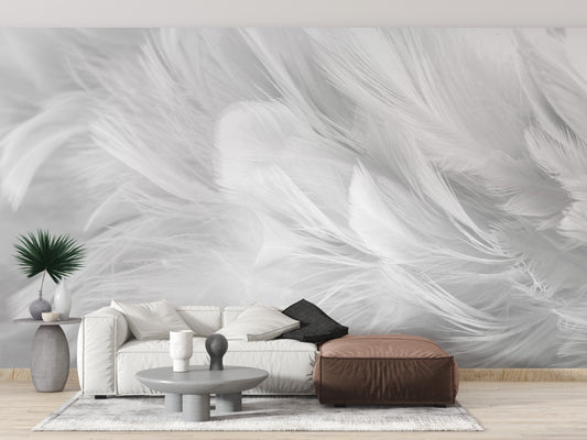 White Bird Feather wallpaper mural in soft white plumes behind a white sofa and brown leather pouf in a living room